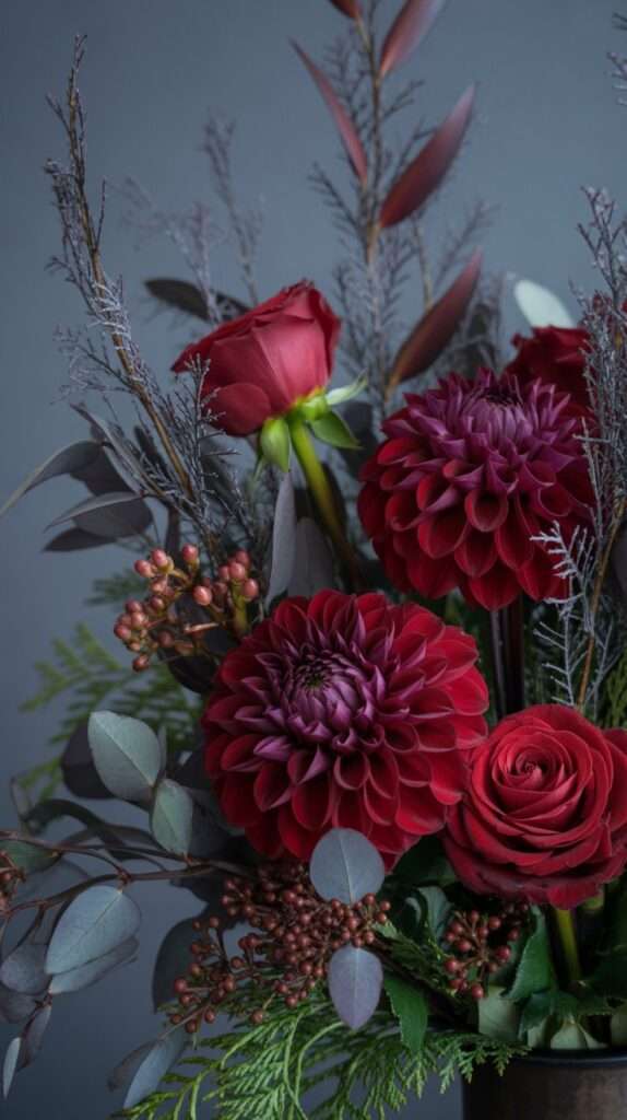 “Dramatic winter floral arrangement with burgundy dahlias, red roses and dark foliage, styled in moody lighting for a rich seasonal look.”